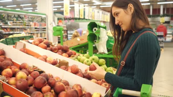 Приваблива молода жінка вибирає яблуко на ринку фруктових овочів — стокове відео