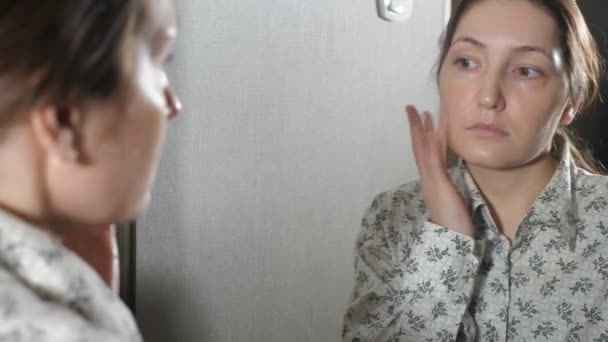 Das Porträt einer jungen Frau mit Haut, die ihr Gesicht mit einer Creme eincremt — Stockvideo