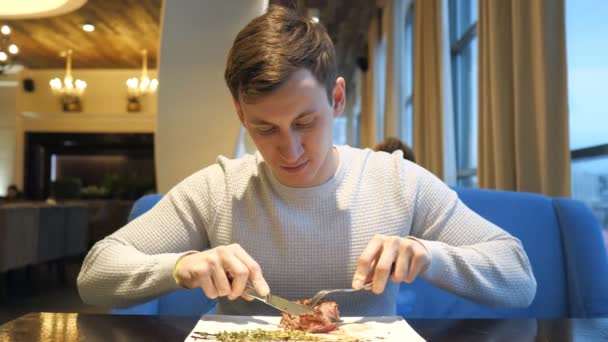 Jovem cortando carne carne bife comer apreciando o jantar no restaurante — Vídeo de Stock