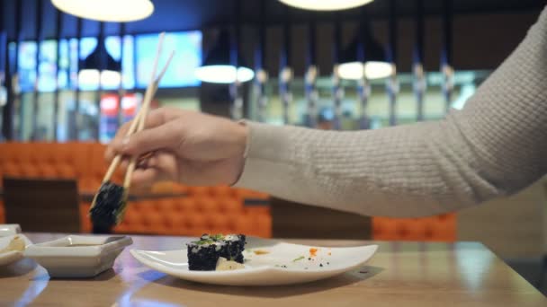 Jovem casal com pauzinhos leva sushi de um prato em um restaurante japonês . — Vídeo de Stock