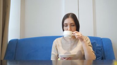 Genç güzel kadın ile fincan çay veya kahve ve gulping kafede oturur