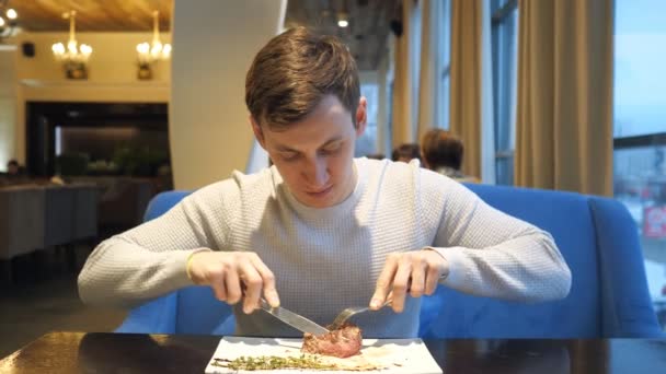 Jonge man heerlijk rundvlees biefstuk knippen met mes en vork eten in café na het werk — Stockvideo