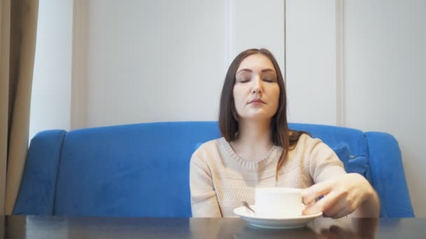 Junge hübsche Frau sitzt im Café mit einer Tasse Tee oder Kaffee und schluckt — Stockvideo