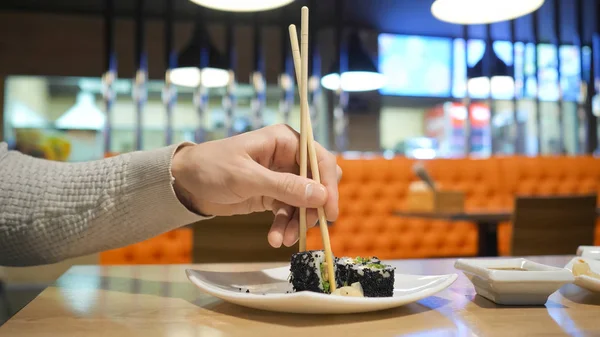 拿着筷子的年轻人在日本餐馆的盘子里吃寿司 — 图库照片