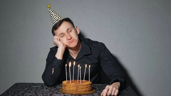 Só o homem celebra umas férias, senta-se sozinho a uma mesa com um bolo e umas velas — Fotografia de Stock