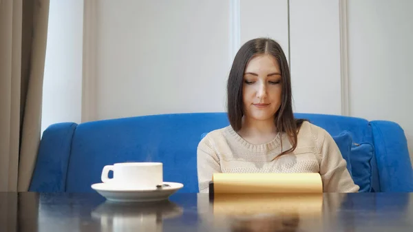 Молодая женщина в кафе выбирает ланч, листая меню — стоковое фото