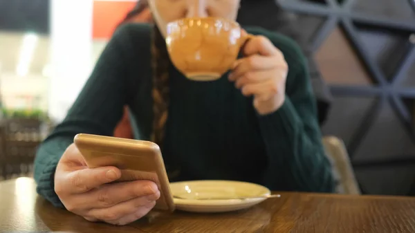 手机在女孩的手在焦点, 女人喝咖啡在模糊的背景 — 图库照片