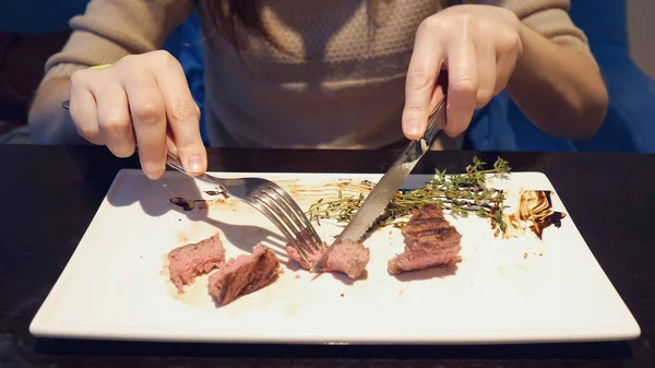 Menina corta um pedaço de bife no prato e come no café — Fotografia de Stock