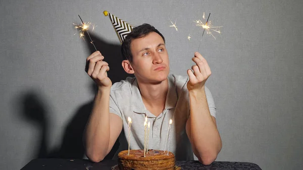 Triste homem solitário em chapéu de festa celebrando aniversário sozinho e segurando o sparkler — Fotografia de Stock