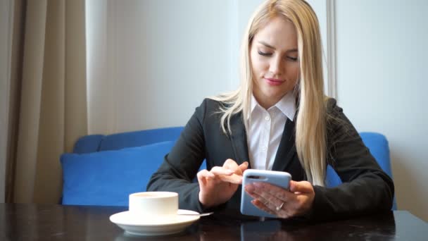 Блондинка в костюмі з телефоном сидить за столом у кафе — стокове відео