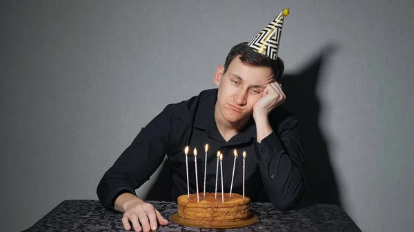 Hombre solo celebra una fiesta, se sienta solo en una mesa con un pastel y una vela —  Fotos de Stock