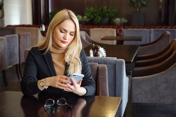 blonde business woman in suit with phone sitting at a table in a cafe