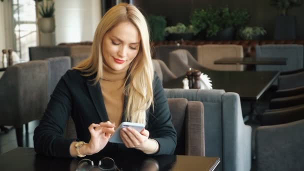 Mulher de negócios em terno com telefone sentado em uma mesa em um café — Vídeo de Stock