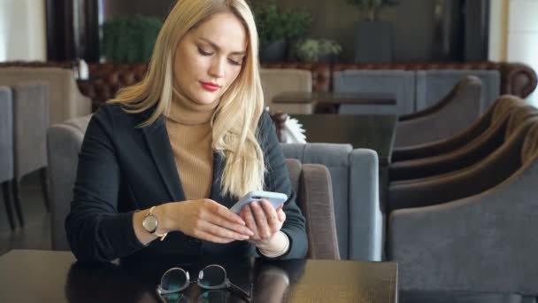 Mujer de negocios en traje con teléfono sentado en una mesa en un café — Vídeos de Stock