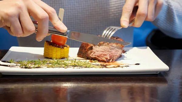 man cuts off a piece of steak and eats in cafe