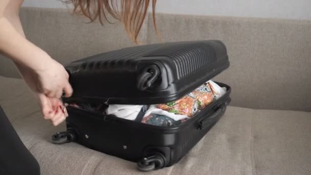 Девушка случайно собирает вещи и пытается закрыть переполненный чемодан . — стоковое видео
