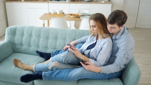 Chico y chica sentarse en el sofá navegar por Internet en los teléfonos inteligentes — Vídeos de Stock