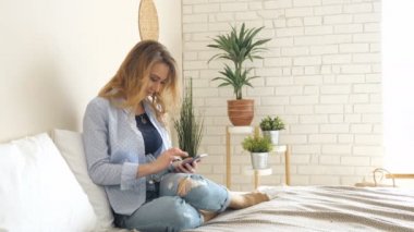 sarışın kız kot pantolon smartphone üzerinde çalışma yatakta oturur