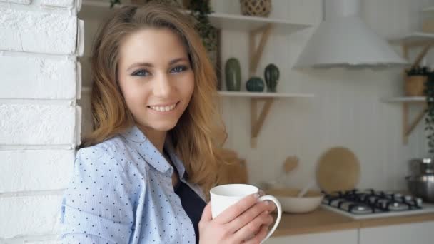 Menina com cabelo solto bebidas chá sorrisos encostados na parede de tijolo — Vídeo de Stock
