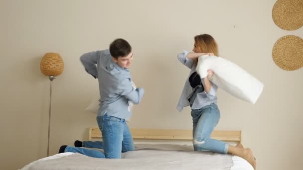 Couple riant se bat avec des oreillers debout sur les genoux sur le lit — Video