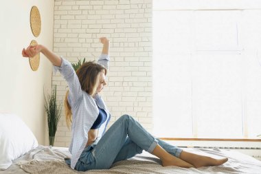 Kız kot pantolon ayakları ellerini uzanan yatakta oturur