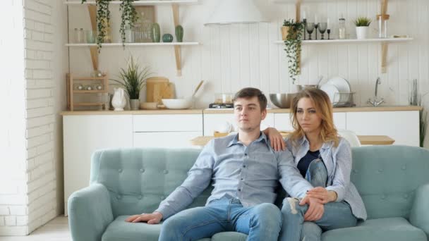 Casal senta-se no sofá azul acolhedor assistindo TV na cozinha moderna — Vídeo de Stock