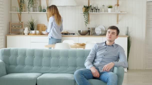 Bonita esposa coloca mesa marido senta-se no sofá assistindo TV — Vídeo de Stock