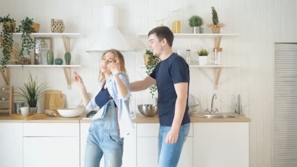 Feliz pareja joven bailando en la cocina vistiendo jeans de baile — Vídeos de Stock