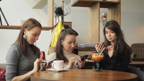 Tři kamarádky ženy v kavárně procházení jejich mobilních telefonů. Přátelské setkání v kavárně — Stock video