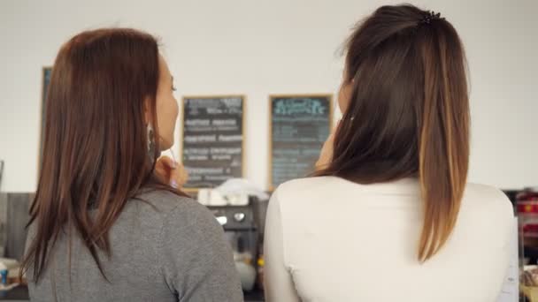 Две женщины обсуждают меню и выбирают еду в кафе, стоящем у барной стойки . — стоковое видео