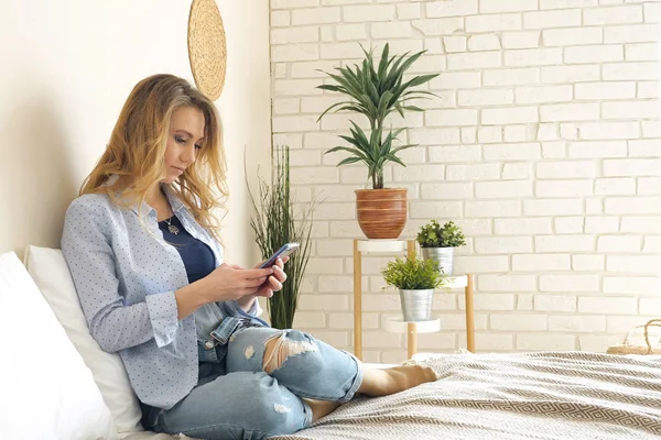 sarışın kız kot pantolon smartphone üzerinde çalışma yatakta oturur