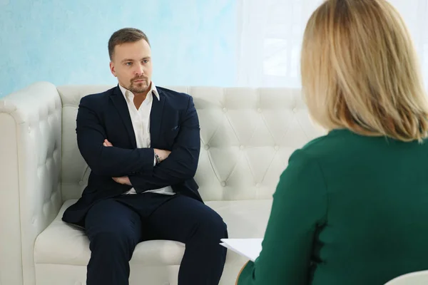 Homem de negócios irritado sentado no sofá falando com psicólogo feminino — Fotografia de Stock