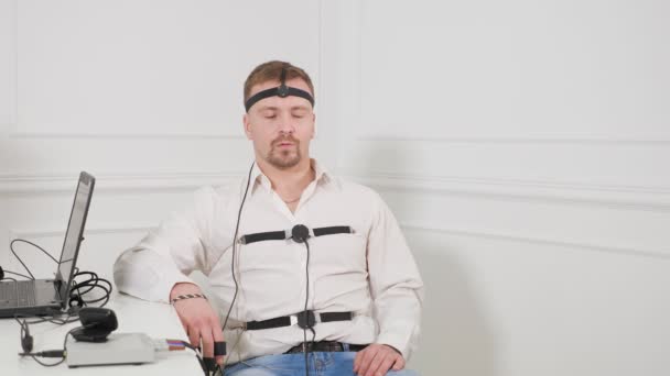 A man answers the questions of the expert polygraph sitting on a chair in an office — Stock Video