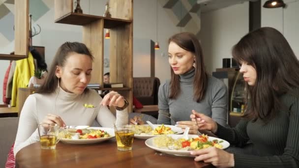 Tres amigas están comiendo juntas en la cafetería y hablando, disfrutando de su comida . — Vídeos de Stock