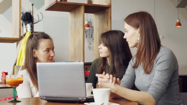 Colegas mujeres discuten proyecto conjunto en la cafetería en el centro de coworking utilizando un ordenador portátil . — Vídeos de Stock