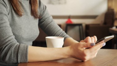 Kadın kafe ve okuma şey içinde hareket eden telefon içinde kahve içiyor. Telefon yakın çekim ile el.