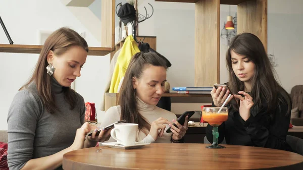 Drei Freundinnen in einem Café surfen auf ihren Mobiltelefonen. Freundschaftstreffen im Café — Stockfoto