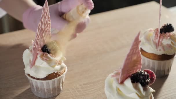 Bäcker sprüht goldene glitzernde Cupcakes. — Stockvideo