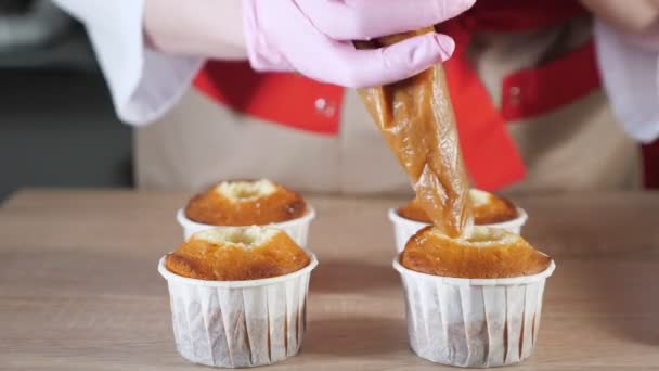 Pasticcere riempie muffin in bicchieri di carta ripieno di caramello con sacchetto di pasticceria — Video Stock