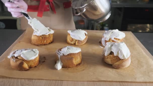 Femme boulanger chef frottis crème sur rouleaux de cannelle fraîche cuite au four . — Video