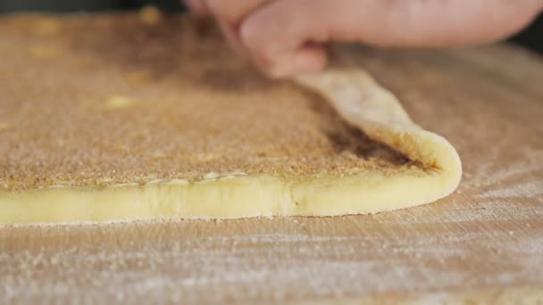 Baker chef enrolla la masa con canela, azúcar y mantequilla en un rollo sobre la mesa . — Vídeos de Stock