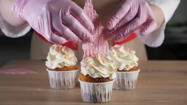 Випічка шеф-кухаря прикрашає кекси з вершками в паперових стаканчиках вафельними. Рука крупним планом . — стокове відео