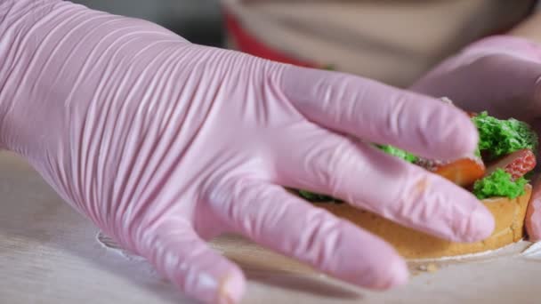 Σεφ ζαχαροπλαστικής σε λαστιχένια γάντια δείχνει την πλήρωση της κοπής σε μισό φράουλα μίνι κέικ. — Αρχείο Βίντεο