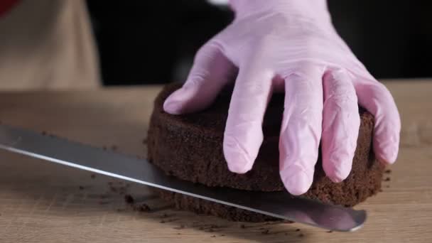 Pastry chef is cutting chocolate sponge cake on slices with big knife. — Stock Video