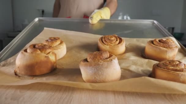 Cukrárna umisťuje čerstvě pečené skořicí cívky na stůl z pečicího talíře. — Stock video