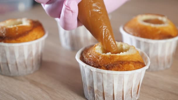 Pasticcere riempie muffin in bicchieri di carta ripieno di caramello con sacchetto di pasticceria . — Video Stock