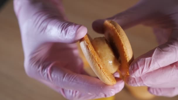 Chef de pastelaria está enchendo macaroons de limão com creme usando saco de confeitaria . — Vídeo de Stock