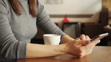 Kadın kafede bir fincan kahve içiyor ve telefonda bir mesaj yazarak