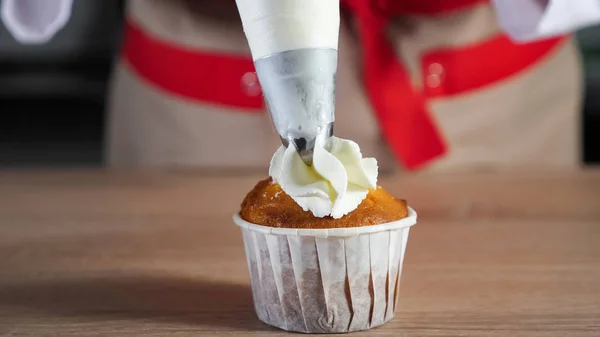 Konditor dekoriert Muffin in Pappbechern weiße Sahne mit Teigtasche. — Stockfoto