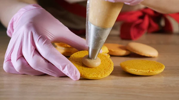 Chef de pastelaria está enchendo macaroons de limão com creme usando saco de confeitaria . — Fotografia de Stock